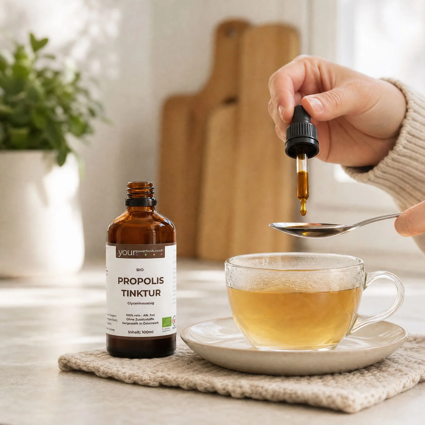 Propolis Tinktur, alkoholfrei, 100 ml – braune Tropfflasche neben Teetasse, Hand tropft Tinktur auf Löffel