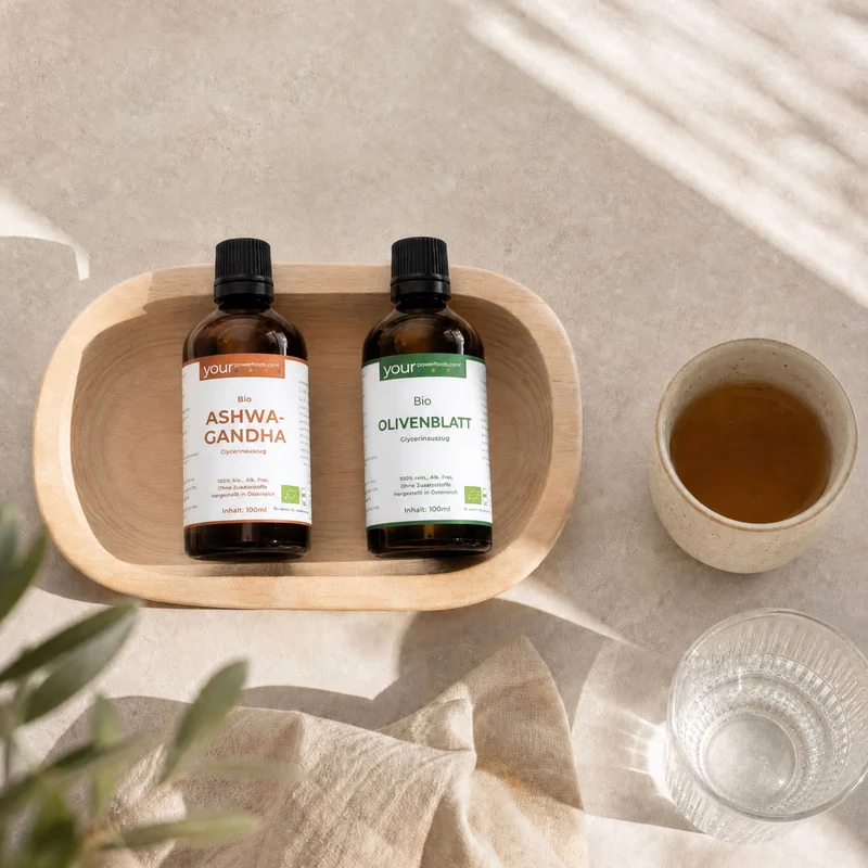 Balance Blutdruck-Bundle – zwei braune Tropfflaschen Bio Ashwagandha und Bio Olivenblatt in einer Holzschale, daneben Tee und